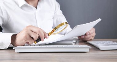 Elinde belgeli büyüteç tutan adam..