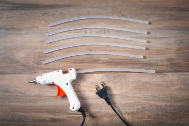 Tahta zemin üzerinde plastik çubuklar olan beyaz yapıştırıcı tabancası..