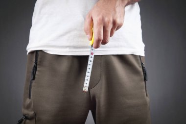 Man with a measuring tape measures his penis size.