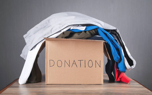 Donation box with clothes on the wooden table.