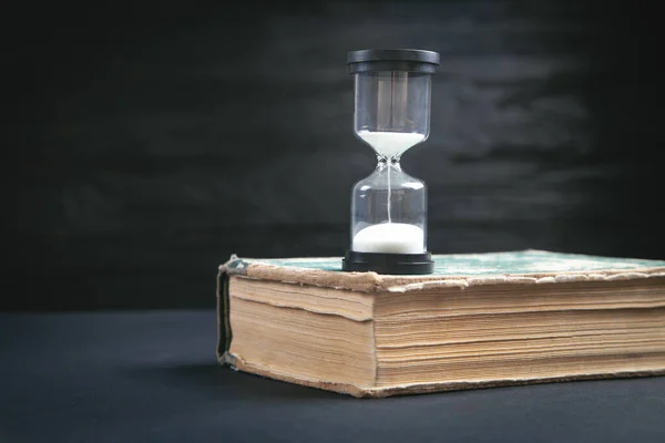 Buch Und Sanduhr Auf Dem Schwarzen Tisch — Stockfoto