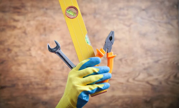 Worker hand holding level, wrench, pliers. Working tools
