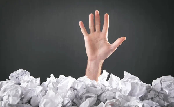 Male hand reaches out from heap of crumpled papers.
