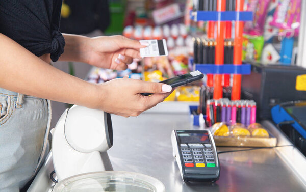 Caucasian woman using smartphone and holding credit card in supermarket.