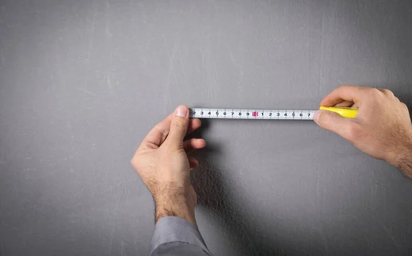 Man measures a gray wall with measuring tape.