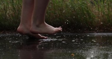 Yağmurda çıplak ayakla su birikintilerinde atlayan kız. Mutlu çocukluk, mutluluk.