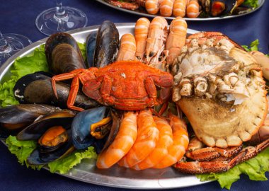 Mavi masa örtüsünde deniz ürünleri tabağı. Midye, karides, kahverengi yengeç, örümcek yengeci ve Norveç ıstakozu.  