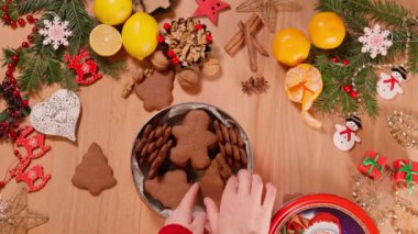 Bir kızın elleri bir Noel kutusunu açar ve Noel süslemeleri ve şenlikli yiyeceklerle süslenmiş bir masaya zencefilli kurabiye serer.