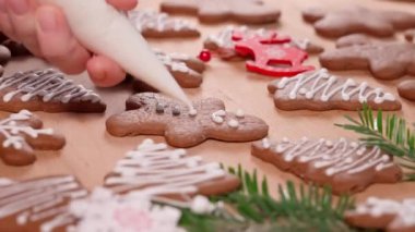 Noel kurabiyelerinin üzerine beyaz krema çizmek, yeni yıl süslemeleri ile süslenmiş masa.