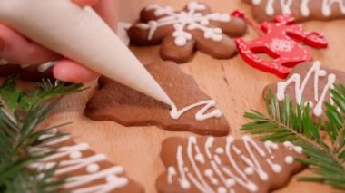 Noel kurabiyelerinin üzerine beyaz krema çizmek, yeni yıl dekorasyonlarıyla süslenmiş masa, ön manzara.