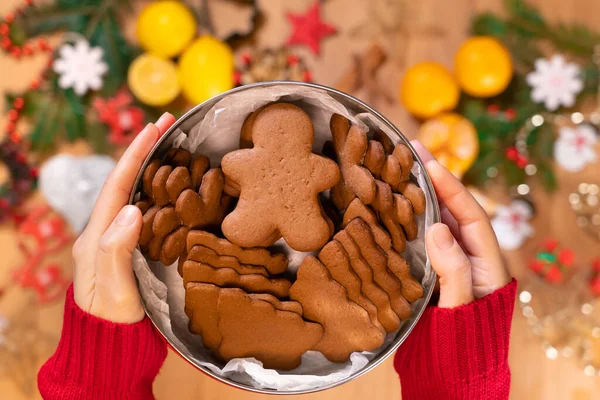 Bir kızın elinde Noel kurabiyesiyle dolu bir kutu. Yeni yıl dekorunun arka planında, yakın planda, en üstte.