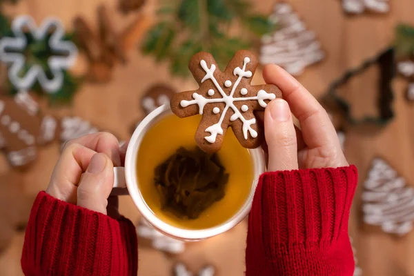 Noel süslemelerinin arka planında bir fincan yeşil çay ve Noel zencefilli ekmeği olan bir kızın elleri.