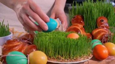 Paskalya yumurtalarını yeni yetişmiş buğday filizlerine koyan kadın elleri ev yapımı paskalya tavşanlarıyla süslenmiş masa, ön manzara.