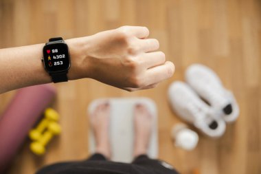 Kalp atış hızı, basamaklar ve yanık kalorileri gösteren fitness izleyicisine bakıyorum. Kadın eli için akıllı saat, bakış açısı, evde formda kalma konsepti, kapalı alanda egzersiz.