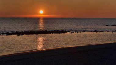 Sahilde minimalist altın gün batımı. Güzel ışıklar kayalıklar arasındaki deniz suyunu yansıtıyor. Ta ki gökyüzüne kadar..