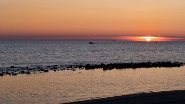 Sahilde muhteşem bir pastel gün batımı altın gibi berrak bir gökyüzü ve gölgeli turkuaz deniz ufuk güneşiyle deniz yüzeyinde oturan balıkçı tekneleri.
