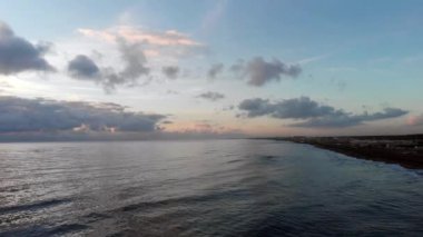 Roma denizi üzerinde 4k drone 'la geriye doğru uçar ve kumsalda koyu kum ve köpüklü dalgalarla dolaşır.