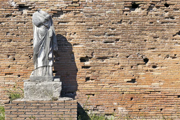 Ancient Roman art with ruin of marble statue dressed with toga with background a well preserved ancient brick wall, located at Ostia Antica, Rome.