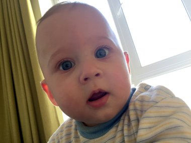 Renkli fotoğraf için poz veren çocuk yüzlü güzel bir oğlan. Cadre, çocuk görünümlü bir erkek bebekten, beyaz bir yüz ifadesinden oluşuyor. Sağlıklı erkek bebek, çocuk yüzü. İyi bir atış için rahatlıyor..