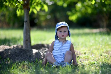 Renkli fotoğraf için çocuk bahçesinde poz veren güzel bir erkek bebek. Cadre, çocuk bahçesindeki erkek bebekten, beyaz bir yüz ifadesinden oluşuyor. Sağlıklı erkek bebek çocuk bahçesinde iğne için dinleniyor..