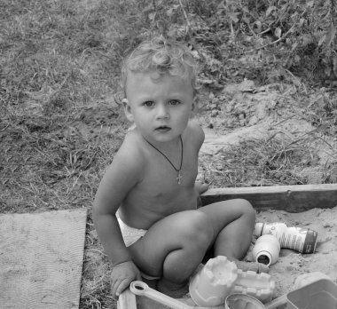 Kum havuzunun yanında fotoğrafçı pozu veren güzel bir bebek. Bebek kum havuzundaki kuru kum tanelerinden oluşur. Küçük çocuklar için ev yapımı kum havuzu. Kumlu bebek kum havuzu, kum havuzu ve çocuk oyunu..