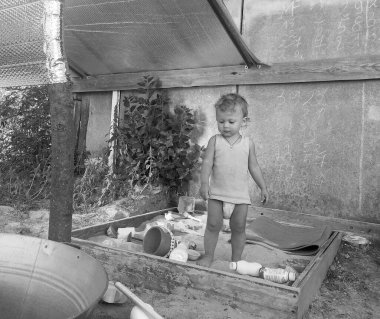 Kum havuzunun yanında fotoğrafçı pozu veren güzel bir bebek. Bebek kum havuzundaki kuru kum tanelerinden oluşur. Küçük çocuklar için ev yapımı kum havuzu. Kumlu bebek kum havuzu, kum havuzu ve çocuk oyunu..
