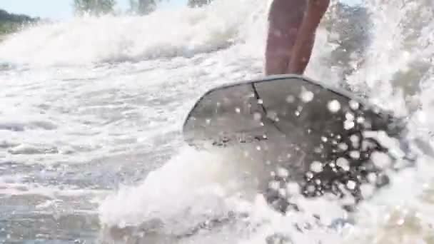Серфер, прыгающий на скорости в волнах с помощью вейкборда, выплескивает на камеру капли воды — стоковое видео