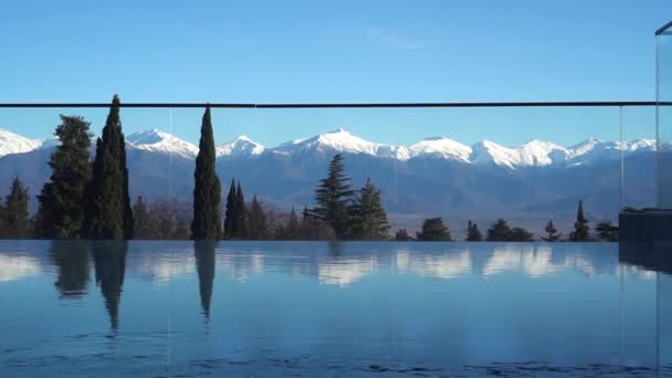 度假胜地的室外游泳池 山景全景 山顶上的雪 蓝色水面上的树木和山峰的反光 阳光灿烂的旅行日 — 图库视频影像