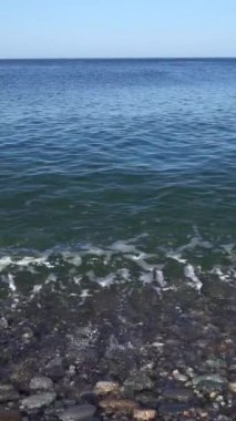 Güneşli bir günde deniz sörfü. Işık dalgaları, çakıl taşı kıyısı. Sahilde çok renkli ıslak çakıl taşları