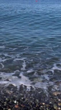 Güneşli bir günde deniz sörfü. Işık dalgaları, çakıl taşı kıyısı. Sahilde çok renkli ıslak çakıl taşları