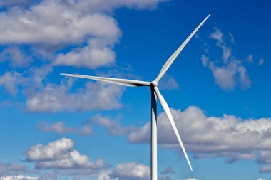 Parlak mavi gökyüzüne ve beyaz bulutlara karşı yel değirmeni. Çevre dostu elektrik kaynağı