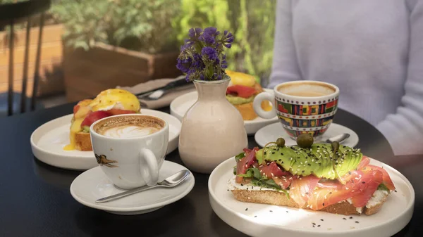 Somon ve avokado ile güzel dekore edilmiş tost, yumurtalı benedict ve cappuccino Kahvaltı toplantılar için gidiş zamanıdır. 