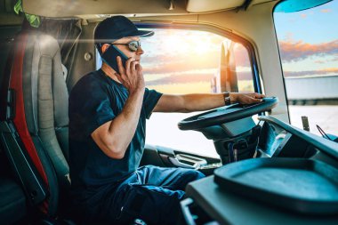 Yakışıklı, orta yaşlı, profesyonel bir kamyon şoförünün portresi. Tehlikeli bir şekilde akıllı telefonunu araba kullanırken biriyle konuşmak için kullanıyor..