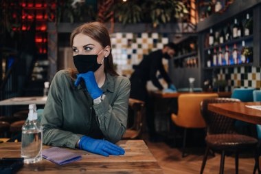 Genç restoran çalışanları Coronavirus salgınına karşı masaları temizleyip dezenfekte ediyorlar. Koruyucu maske ve eldiven takıyorlar..