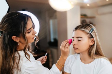 Makyaj yaparken genç ve güzel bir kadının yüzünü yakından çek. Sanatçı göz farı tabanını fırçayla kullanıyor. Profesyonel güzellik uzmanı işi.. 