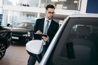 Galeride çalışan araba satıcısı ve araba detaylarını son kez kontrol ediyor alıcı gelmeden önce..