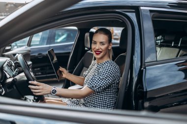 Kullanılmış araba satıcısı olarak çalışan güzel bir genç kadın. Müşteri veya alıcıdan önce dijital tablet kullanıyor ve araba durumunu kontrol ediyor. Kullanılmış araç galerisi.