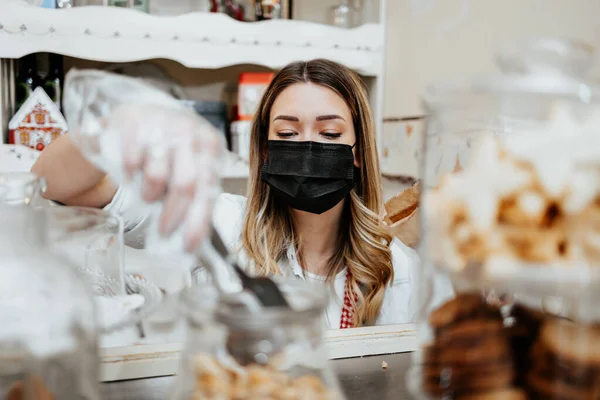 과자가게 가게에서 얼굴을 보호하는 마스크를 아름다운 판매업자 맛있는 과자를 포장하고 — 스톡 사진