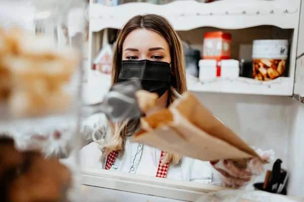 과자가게 가게에서 얼굴을 보호하는 마스크를 아름다운 판매업자 맛있는 과자를 포장하고 — 스톡 사진