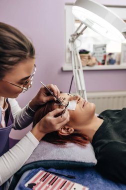 Kirpik uzatma prosedüründeki güzel kızıl saçlı kadın. Kozmetik ve vücut bakımı yakın çekim. Sığ alan derinliği ve seçici odak.