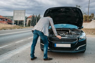 Orta yaşlı şık bir işadamı araba arızasını veya motor arızasını düzeltmeye çalışıyor ve yolda araba kazası için çekici servisi bekliyor. Yol kenarı yardım kavramı.