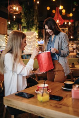 Alışveriş yaptıktan sonra kafeteryada ya da restoranda oturup mutlu mesut sohbet eden iki arkadaş. Ayrıca birbirlerine aldıkları kıyafetleri de gösteriyorlar..