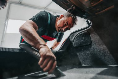 Profesyonel işçi arabasının içini ve bagajını elektrikli süpürgeyle temizliyor, araba temizleme (ya da valelik) konsepti. Seçici odaklanma. Ultra geniş açı..