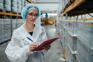 Tıbbi malzeme araştırma ve üretim fabrikasında çalışan ve sevkiyattan önce damıtılmış su dolu kutuları kontrol eden koruyucu işçi. Denetleme kalite kontrolü. Sanayi deposu.