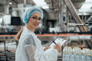 Tıbbi malzeme araştırma ve üretim fabrikasında çalışan ve sevkiyattan önce damıtılmış su kutularını kontrol eden koruyucu işçi. Denetim kalite denetimi. 