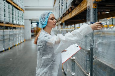 Tıbbi malzeme araştırma ve üretim fabrikasında çalışan ve sevkiyattan önce damıtılmış su dolu kutuları kontrol eden koruyucu işçi. Denetleme kalite kontrolü. Sanayi deposu.