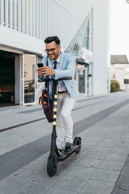 Şehir caddesinde elektrikli scooter kullanan ve kullanan genç modern bir adam. Modern ve ekolojik ulaşım kavramı. 