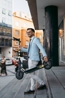 Şehir caddesinde elektrikli scooter kullanan ve kullanan genç modern bir adam. Modern ve ekolojik ulaşım kavramı. 