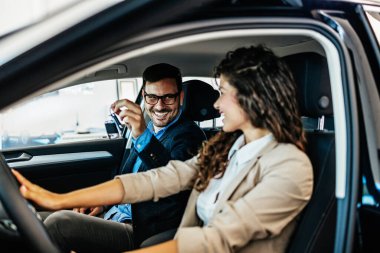 Mutlu orta yaşlı çift, galeride yeni araba seçerken ve alırken eğleniyor. Arabanın içinde oturuyorlar..