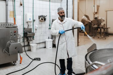 Orta yaşlı erkek, endüstriyel mezbahada çalışıyor ve günlük işini bitiriyor. Gıda işleme tesisi zeminini ve makine üretim hatlarını suyla temizliyor ve yıkıyor..